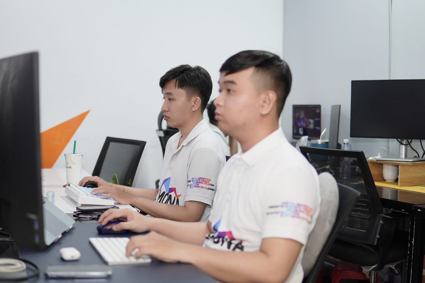 Hai lập trình viên MONA mặc áo THE MONA đang viết phần mềm